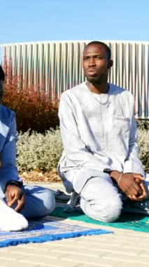 Geleneksel Dashiki giysileri giyen iki Senegalli Müslüman dışarıda dua ediyorlar.