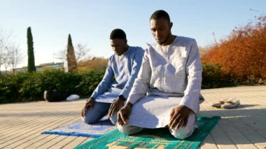 Senegalli iki genç adam geleneksel Dashiki kıyafetleri giyer, dua halıları üzerinde diz çöker ve muhtemelen ramazan boyunca dışarıda dua ederler.