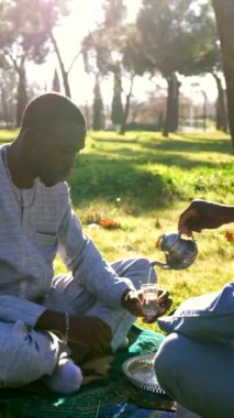 Dashiki giyen Senegalli adamın geleneksel çayı, güneşli park ortamında yeşil manzaralı seremoni sırasında kültürel içeceği paylaşmak.