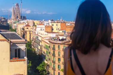 Barselona 'nın panoramik manzarasından hoşlanan genç bir kadın, Sagrada familia da dahil, aydınlık bir yaz gününde, şehir güzelliğini ve seyahat deneyimini gözler önüne seriyor.
