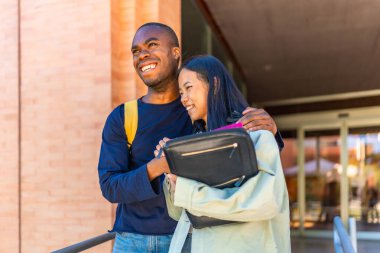 Afrikalı gülümseyen genç bir adam üniversitenin girişinde Çinli bir bayan arkadaşını kucaklıyor ve tebrik ediyor.