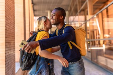 Üniversite kampüsünde kucaklaşırken ve selamlaşırken çok ırklı öğrenciler mutlu bir şekilde gülümsüyor.