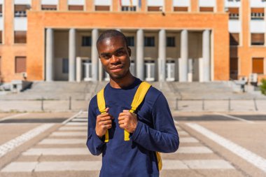Sırt çantası taşıyan Afrikalı üniversite öğrencisi üniversite binasının yanında poz veriyor.