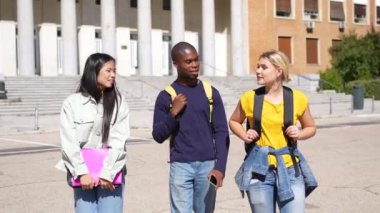 Üç üniversite öğrencisinin not defterleri ve sırt çantasıyla kampüs boyunca yürüdükleri yatay uzunlukta videolar.