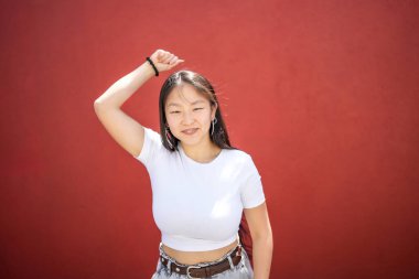 Asyalı kadın Han 'ı güneşin altında kırmızı bir duvara karşı K-pop dansı yaparken yetiştiriyor.