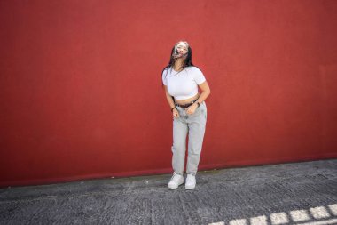 Şehirli genç Asyalı şehir dansçısı güneşli bir günde şehir kırmızı duvarının yanında gösteri yapıyor.