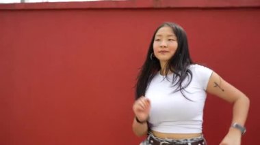 Kırmızı bir duvarın karşısında K-pop koreografisi dans ederken Asyalı genç şehir dansçısı gölgeli boks yapıyor.