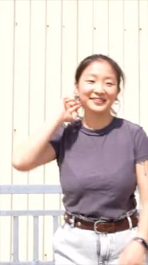 Endüstriyel bir binanın yanında dans eden Asyalı genç bir kızın dikey videosu.