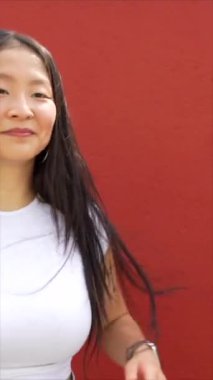 Genç Asyalı kadın güneşin altında kırmızı duvarın yanında dans eden K-pop koreografisi