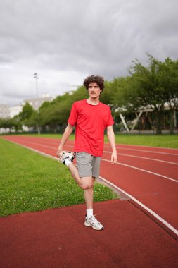 Genç bir beyaz erkek koşucunun dikey uzunluğu koşu pistinde bacaklarını esnetiyor.