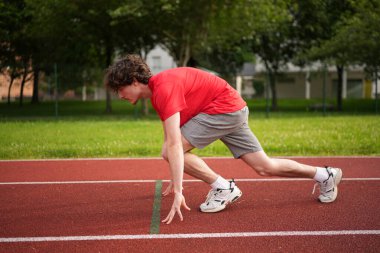 Beyaz tenli genç bir koşucunun yan görünümü bir pistin başlangıç çizgisinde koşmaya hazır.