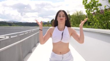 Beyaz, genç, sportif bir kadın. Şehvetli bir şekilde kameraya bakıyor. Açık bir köprüde şehir dansı yapıyor.