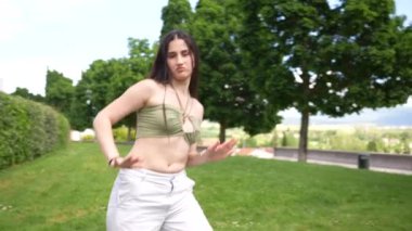 Genç atletik beyaz kadın parkta dans ederken çömeliyor.