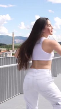 Modern şehir müziğinin önünde diz çökmüş beyaz tenli genç bir kadının dikey videosu.