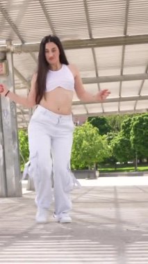 Parkta serbest dans eden beyaz elbiseli, havalı bir kadının yan görüntüsü.