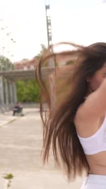 Şehir parkında dans eden beyaz, kendine güvenen bir kadının düşük açılı fotoğrafı.