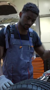 Tamirci garajdaki bir arabanın lastik basıncını kontrol ediyor. Aracın bakımını ve güvenliğini sağlıyor.