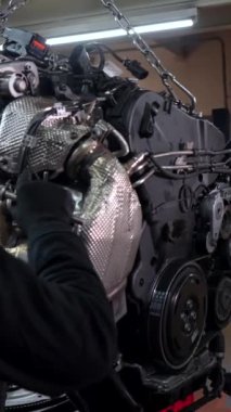 Garajdaki asansörden askıya alınmış bir araba motoru üzerinde çalışan tamirciler, kurulum ve onarım görevlerine odaklanıyorlar.