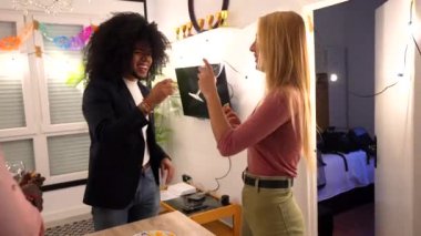 Çok ırklı arkadaşlar bir evde toplanma partisinde içki ve atıştırmalıkların keyfini çıkarırken gülüp sohbet ediyorlar.