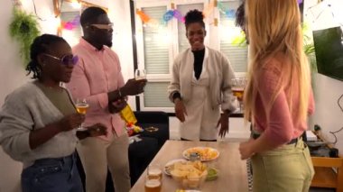 Çok ırklı arkadaşlar, neşeli bir evde buluşmalarını kutlarken içki ve atıştırmalıkların keyfini çıkarırlar.