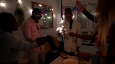 Çok ırklı arkadaşlar evde parti veriyor, maytap tutuyor ve birlikte kutluyorlar.