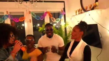 Karaokeyi seven, şarkı söyleyen ve dans eden çok ırklı arkadaşlar neşe ve heyecan dolu bir ev partisinde