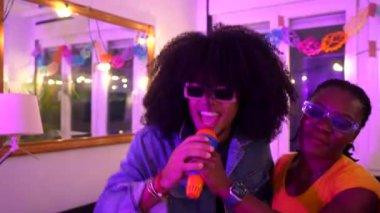 Çok ırklı arkadaşlar canlı bir ev partisinde karaokeyi seviyorlar, birlikte şarkı söylüyorlar ve neşeli anılar yaratıyorlar.