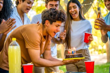 Doğum günü pastasıyla parkta arkadaşlarıyla kutlama yapan mutlu genç adam.