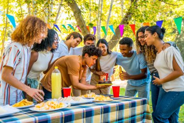 Genç adam, parkta çok ırklı arkadaşlarla piknik yaparken doğum gününü kutluyor.