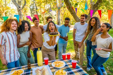 Kafkasyalı genç bir kadın parkta çeşitli arkadaşlarla doğum günü pastası mumları üflüyor.
