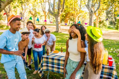 Afrikalı bir kadının gözlerini kapayan çok ırklı arkadaşlar parkta ona doğum günü hediyesiyle sürpriz yaptılar.