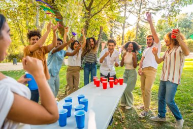 Parti sırasında parkta bira pong oynayan çok ırklı öğrenciler.