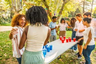 Çok ırklı, mutlu, rahat arkadaşlar güneşli bir bahar gününde parkta bira pong oynuyorlar.