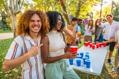 Parkta bira pong oynayarak kazanan Afrikalı bir kadını işaret eden adam.
