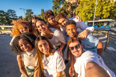 Gün batımında sokakta selfie çeken çok ırklı bir grup mutlu genç arkadaş.