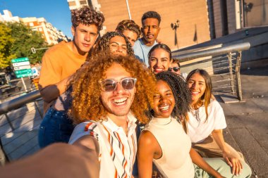 Kıvırcık saçlı ve çok ırklı arkadaşları olan bir adam şehirde selfie çekiyor.