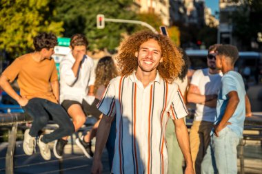 Günbatımında şehirde gülümseyen kıvırcık saçlı ve arkadaşları olan genç bir adamın portresi.
