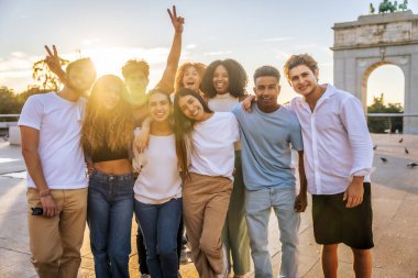 Gün batımında şehirde mutlu mesut duran ve kucaklaşan çok ırklı arkadaşların portresi.