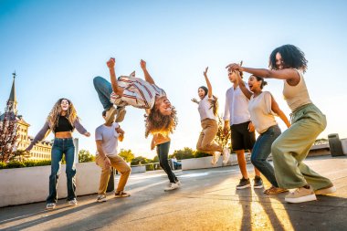 Man jumping dancing free style surrounded by multi-ethnic friends in the city during sunset clipart