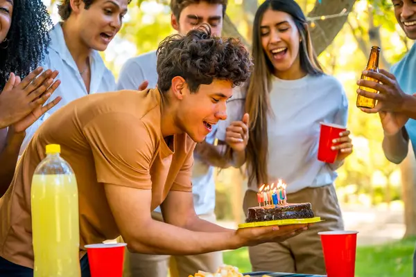Doğum günü pastasıyla parkta arkadaşlarıyla kutlama yapan mutlu genç adam.