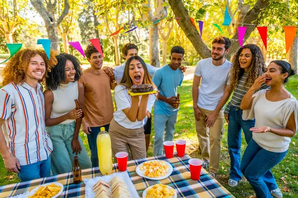 Kafkasyalı genç bir kadın parkta çeşitli arkadaşlarla doğum günü pastası mumları üflüyor.