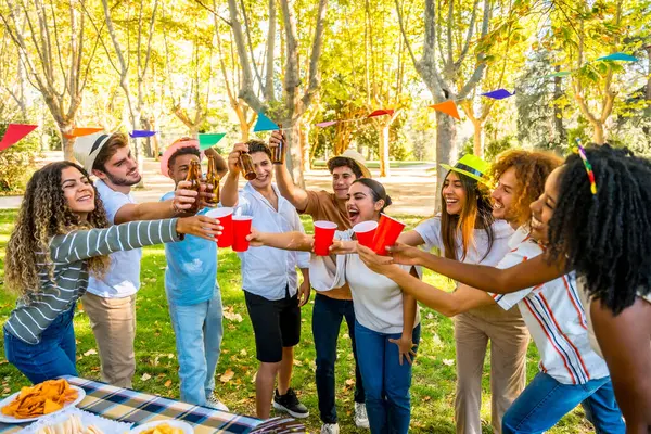 Çok ırklı arkadaşlar parkta piknik yaparak doğum gününü kutluyorlar.