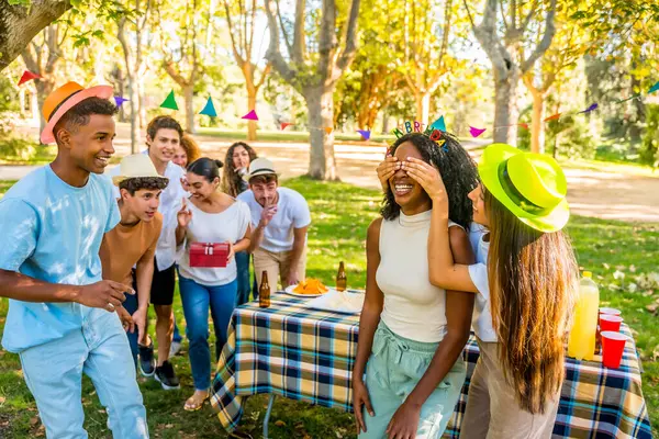 Afrikalı bir kadının gözlerini kapayan çok ırklı arkadaşlar parkta ona doğum günü hediyesiyle sürpriz yaptılar.