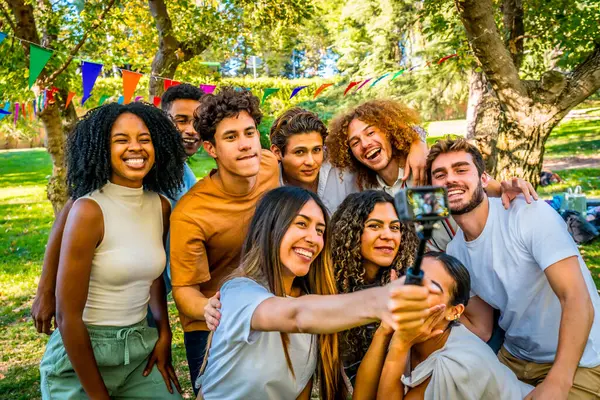 Gülümseyen çok ırklı arkadaşlar parkta doğum gününü kutlarken giyilebilir kamerayla selfie çekiyorlar.