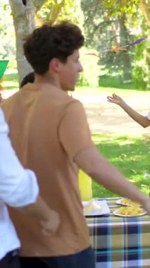 Genç adam, parkta çok ırklı arkadaşlarla piknik yaparken doğum gününü kutluyor.