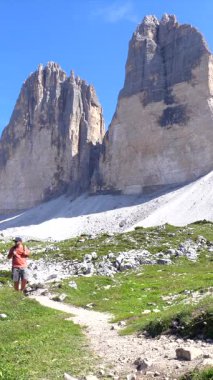 Turist, dolomitlerdeki görkemli Tre cime di lavaredo zirvelerine giden manzaralı bir yolda yaz yürüyüşünün tadını çıkarıyor.