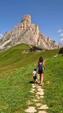 Anne ve oğul, İtalyan dolomitleriyle etkileyici bir giau geçidinde yürüyorlar, yaz tatilinin tadını çıkarıyorlar.