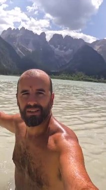 Güneşli bir yaz gününde, soluk kesici dolomitlerle çevrili lago di landro 'nun turkuaz suyunda yüzerken, turist el sallıyor.