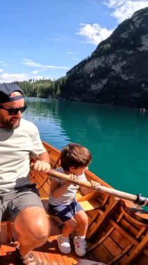 Baba ve oğul, arka planda çarpıcı dolomitlerle birlikte Braies Gölü 'nde tahta bir teknede kürek çekiyorlar.