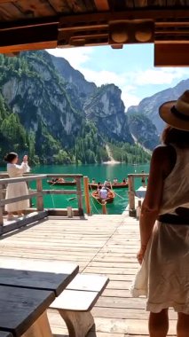 Hasır şapkalı kadın ahşap iskelede duruyor, Braies Gölü 'nün büyüleyici manzarasına ve dolomitlerle çevrili dağlara hayran.